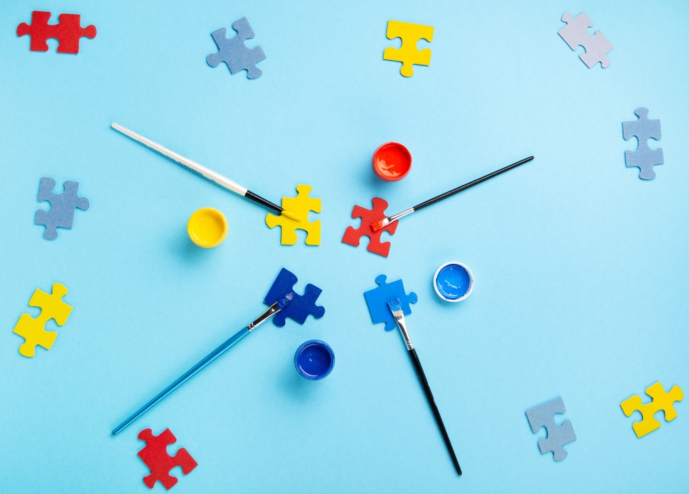 World Autism Awareness Day or month concept. Creative design for April 2. White puzzles, symbol of awareness for autism spectrum disorder and colorful paints on blue background. Top view, copy space.