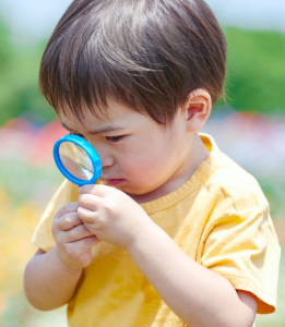 Child in yellow shirt using a magnifying glass
